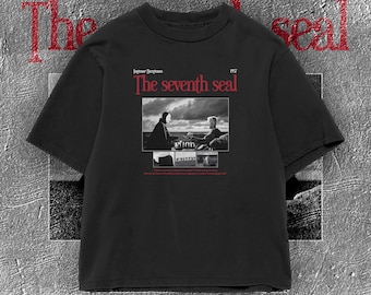 Op de afbeelding: Zwart T-shirt met de rode tekst "The seventh seal" en een zwart-wit afbeelding uit de film. Het shirt bevat ook de naam "Ingmar Bergman" en het jaar "1957".