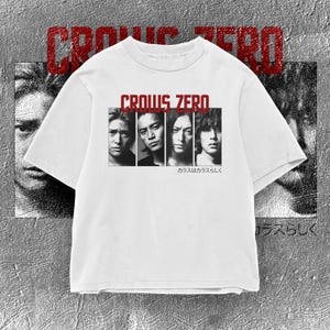 May include: A white short-sleeve t-shirt featuring a graphic print of four men in black and white. Above the portraits, the text reads CROWS ZERO in red. Below the portraits, Japanese text is printed in black. The design is centered on the chest.