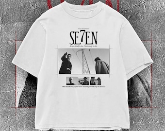 Op de afbeelding: Wit T-shirt met het woord "SE7EN" in een vetgedrukte letter, en een zwart-wit film still graphic. Het shirt bevat ook de tekst "Seven deadly sins, Seven ways to die."