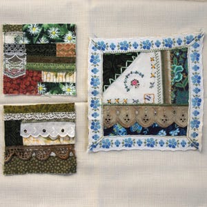 May include: Three small, square fabric art pieces. One features floral and lace details in green, white, and red. Another has a blue floral border and embroidered details. The third has lace and patterned fabric.