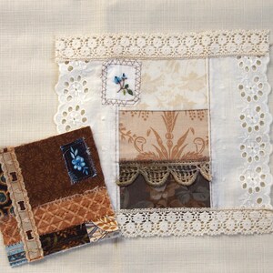 May include: Two handmade fabric items. One is a square patchwork piece with floral and geometric patterns in brown, beige, and white, trimmed with lace. The other is a smaller, rectangular piece with similar patterns and a blue floral accent.