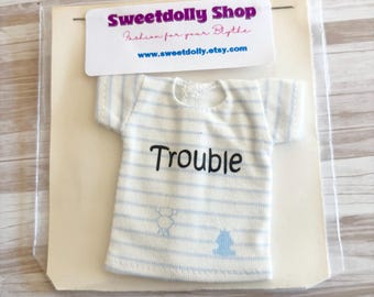 Op de afbeelding: Een miniatuur wit en blauw gestreept t-shirt met het woord "Trouble" in zwart schrift. Het shirt heeft kleine blauwe beer- en boomafbeeldingen. Het shirt is verpakt met een Sweetdolly Shop-label.
