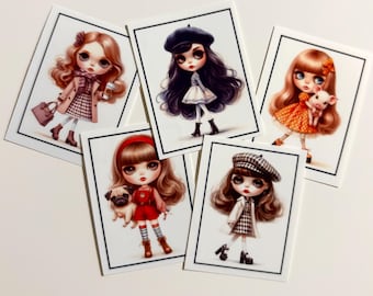 May include: Five rectangular art prints featuring stylized dolls with large eyes. Each print shows a doll in different outfits, including a trench coat, a beret, a polka dot dress with a piglet, red overalls with a pug, and a plaid dress with a cap.