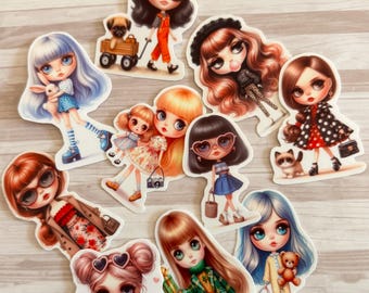 Op de afbeelding: Een verzameling stickers met illustraties van poppen. De poppen hebben grote ogen en verschillende kapsels, gekleed in outfits zoals overalls, jurken en jassen. Sommige poppen houden accessoires vast, zoals een hond, een konijn en een teddybeer.