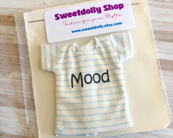 Op de afbeelding: Een miniatuur crèmekleurig T-shirt met lichtblauwe horizontale strepen en het woord "Mood" in zwart. Het shirt is verpakt met een Sweetdolly Shop label.
