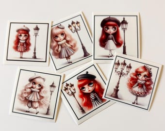 May include: Five square stickers featuring illustrations of dolls with large eyes and long hair, each wearing a beret and standing next to a street lamp. The dolls have red or blonde hair and are dressed in various outfits including striped shirts and skirts.