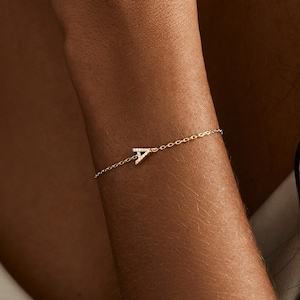 May include: A fine gold chain bracelet with the letter "A" as a charm. The bracelet is a delicate piece of jewellery, with a simple, elegant design. The bracelet is worn on a wrist, suggesting a piece of personalised jewellery.