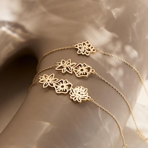 May include: Three gold bracelets with delicate flower cutouts. The bracelets are layered on top of each other, creating a cascading effect.