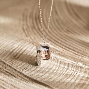 Puede incluir: Collar con colgante de relicario plateado rectangular, abierto para mostrar una fotograf&iacute;a. El colgante mide 16 mm de alto y 10 mm de ancho. El collar cuelga de una fina cadena de plata, una joya personalizada.