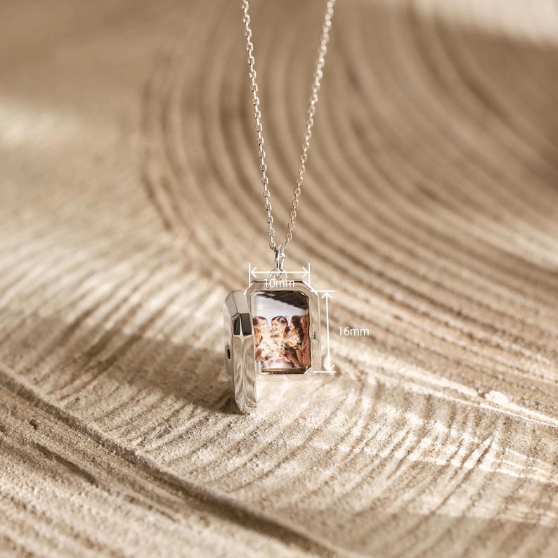 Puede incluir: Collar con colgante de relicario plateado rectangular, abierto para mostrar una fotograf&iacute;a. El colgante mide 16 mm de alto y 10 mm de ancho. El collar cuelga de una fina cadena de plata, una joya personalizada.