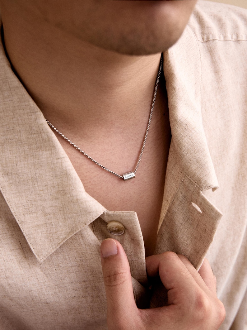 May include: A silver chain necklace with a small rectangular pendant that says "Andrew" on it.