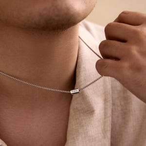 May include: A silver chain necklace with a small, rectangular pendant that says "Andrew" on it.
