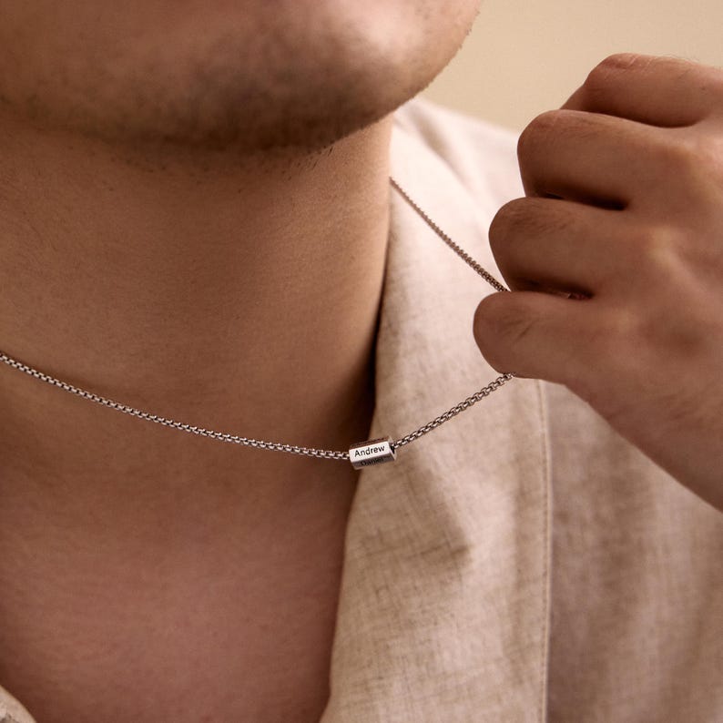 May include: A silver chain necklace with a small, rectangular pendant that says "Andrew" on it.