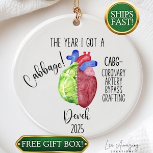 May include: A white ceramic ornament with a gold string. The ornament features a watercolor illustration of a heart and cabbage, with text that reads "The Year I Got a Cabbage!" and "CABG-Coronary Artery Bypass Grafting."