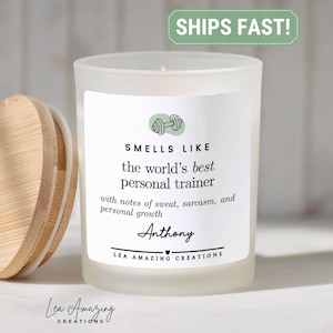 May include: A frosted glass candle with a bamboo lid. The label features a dumbbell icon and the text: SMELLS LIKE the world's best personal trainer with notes of sweat, sarcasm, and personal growth, Anthony, and LEA AMAZING CREATIONS.