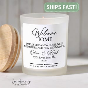May include: A frosted glass candle in a jar with a bamboo lid. The label reads: Welcome HOME, SMELLS LIKE A NEW HOME, NEW MEMORIES, AND NEW BEGINNINGS, Olivia & Mark, 3201 River Bend Dr., 2026, LEA AMAZING CREATIONS. The candle has a single wick.