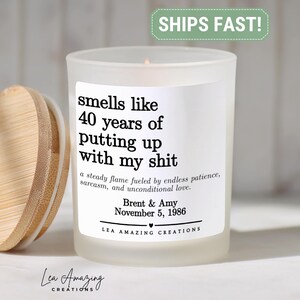 May include: A frosted glass candle with a bamboo lid, featuring a white label with black text that reads: smells like 40 years of putting up with my shit, a steady flame fueled by endless patience, sarcasm, and unconditional love, Brent & Amy, November 5, 1986, LEA AMAZING CREATIONS.