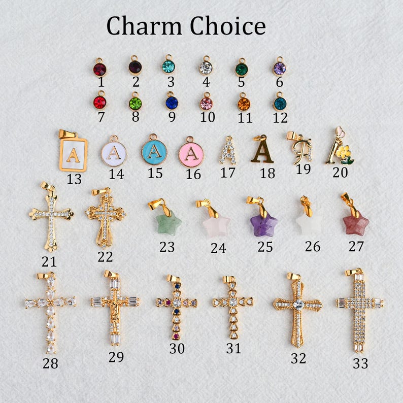 May include: A collection of gold-toned charms, including crosses, stars, and pendants with letters and colorful gemstones. The text "Charm Choice" is at the top. The charms are arranged on a white surface.