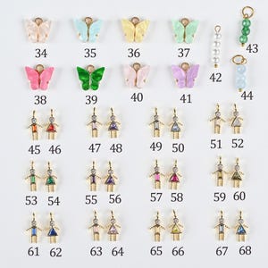 May include: A collection of colorful butterfly and figure-shaped charms with gold-tone metal accents. The charms are in various colors, including pink, green, yellow, and blue. Each charm has a unique design and is numbered for easy selection.