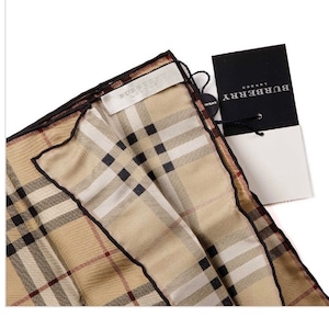 May include: A beige and black plaid silk pocket square with a black trim and a Burberry London tag.