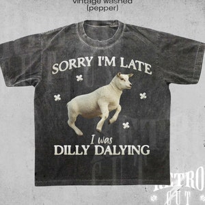 May include: A gray t-shirt with a vintage washed look features a white sheep jumping in the air with the text "Sorry I'm Late I was Dilly Dallying".