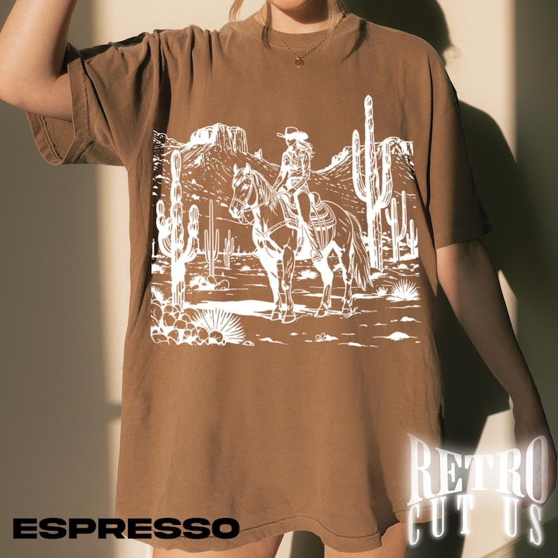 May include: Espresso-colored t-shirt featuring a white graphic of a person riding a horse through a desert landscape with cacti and mountains. The text "ESPRESSO" is at the bottom left. The text "RETRO CUT US" is at the bottom right.