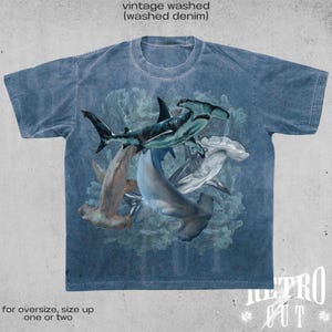 May include: A blue vintage washed denim t-shirt with a graphic print of multiple hammerhead sharks in a swirling pattern. The text "METRO CUT" is printed on the bottom right corner of the shirt.