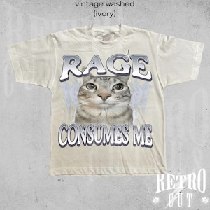 Puede incluir: Una camiseta vintage de color marfil lavado con un gr&aacute;fico de un gato y el texto "RAGE CONSUMES ME".