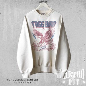 May include: White crewneck sweatshirt with a vintage-style graphic of an eagle with the text "FREE BIRD 1973".