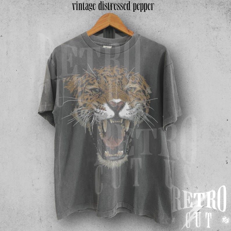 May include: A grey vintage t-shirt with a distressed look featuring a graphic of a snarling jaguar with a black and brown spotted pattern.