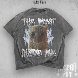 May include: Faded black t-shirt with a distressed graphic featuring a cat's face and the text "THE BEAST INSIDE ME." The shirt has a retro cut design and is made of a soft, comfortable material.