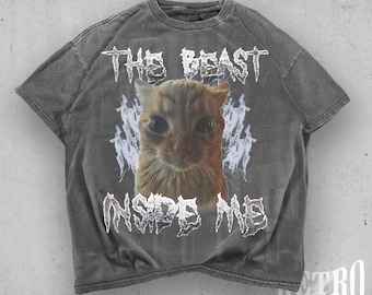 May include: Faded black t-shirt with a distressed graphic featuring a cat's face and the text "THE BEAST INSIDE ME." The shirt has a retro cut design and is made of a soft, comfortable material.
