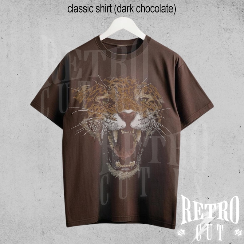 May include: A brown t-shirt featuring a graphic of a snarling jaguar on the front. The shirt has a crew neck and short sleeves. The text "Retro Cut" is printed on the bottom right corner of the shirt.