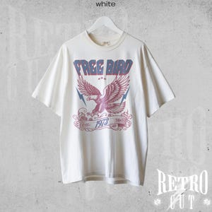 May include: A white t-shirt with a vintage-style graphic of a red eagle with blue wings and the text "FREE BIRD 1973".