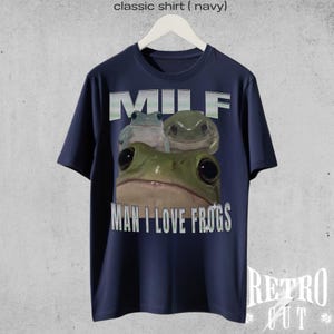 May include: A navy blue t-shirt featuring a graphic of three frogs and the text "MILF MAN I LOVE FROGS".