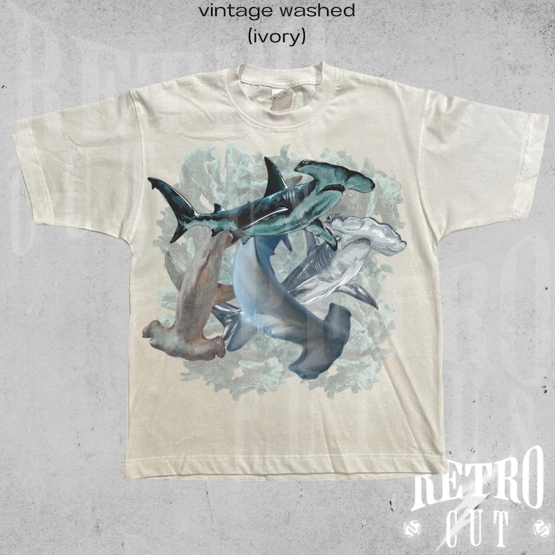 May include: A vintage washed ivory t-shirt with a graphic print of hammerhead sharks in a coral reef setting.