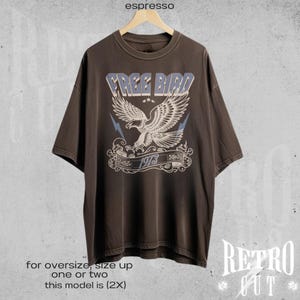 May include: A brown oversized t-shirt with a vintage-style graphic of a blue eagle with the text "FREE BIRD 1973".