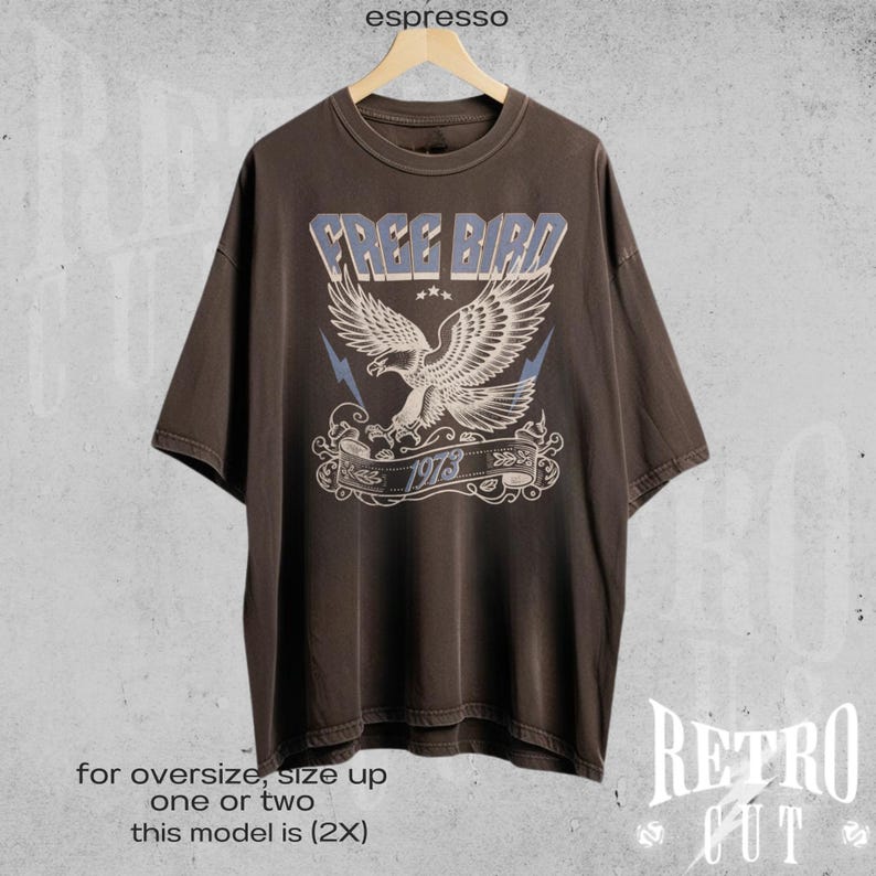 May include: A brown oversized t-shirt with a vintage-style graphic of a blue eagle with the text "FREE BIRD 1973".