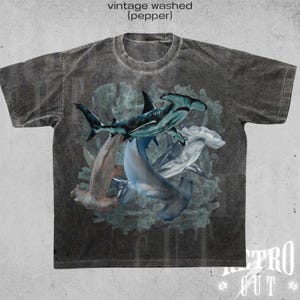 May include: A vintage washed gray t-shirt with a graphic print of four hammerhead sharks in a coral reef. The text "vintage washed (pepper)" is printed at the top of the shirt.