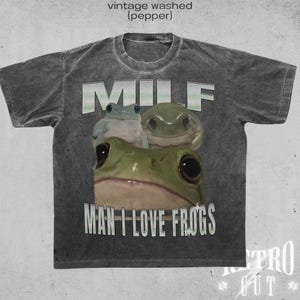 May include: A grey t-shirt with a vintage washed look features the text "MILF MAN I LOVE FROGS" in white. Three green frogs are pictured below the text.