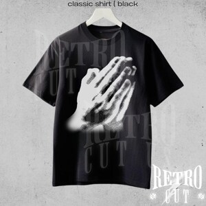 May include: Black classic shirt with a white graphic of praying hands. The shirt has short sleeves and a crew neck. The text "classic shirt (black" is at the top of the image. The brand name "Retro Cut" is at the bottom.