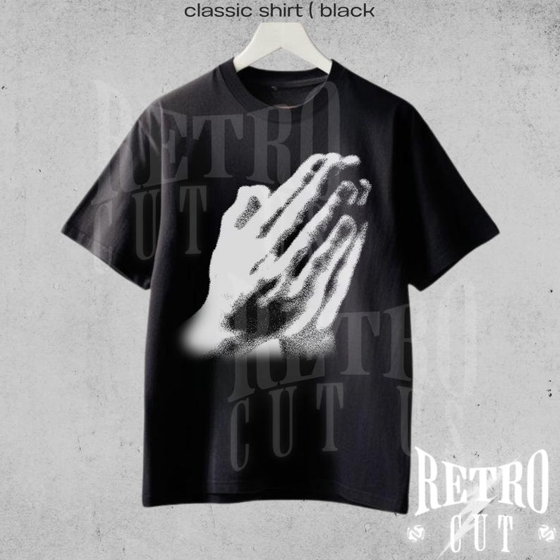 May include: Black classic shirt with a white graphic of praying hands. The shirt has short sleeves and a crew neck. The text "classic shirt (black" is at the top of the image. The brand name "Retro Cut" is at the bottom.