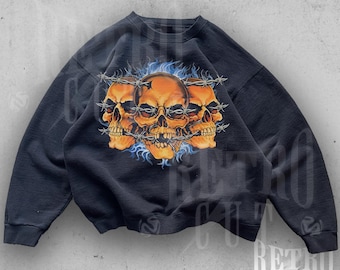 Könnte beinhalten: Schwarzer Pullover mit einem Grafikdruck von drei orangefarbenen Schädeln mit Stacheldraht und blauen Flammen. Der Text "for oversize fit, size up one or two" ist unter dem Grafikdruck gedruckt.