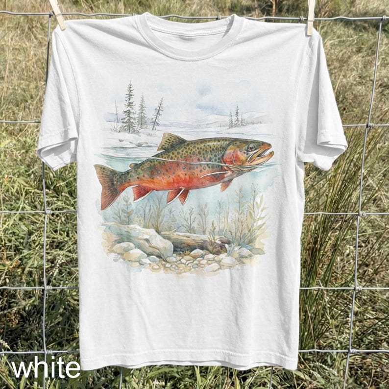 K&ouml;nnte beinhalten: Wei&szlig;es T-Shirt mit einer Aquarellillustration eines Fisches in einem Fluss. Der Fisch hat rote und braune Markierungen. Der Hintergrund zeigt eine verschneite Landschaft und Wasserpflanzen. Das Wort "white" ist unten auf dem T-Shirt aufgedruckt.
