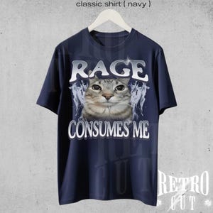 Puede incluir: Una camiseta azul marino con un gr&aacute;fico de un gato y el texto "RAGE CONSUMES ME".