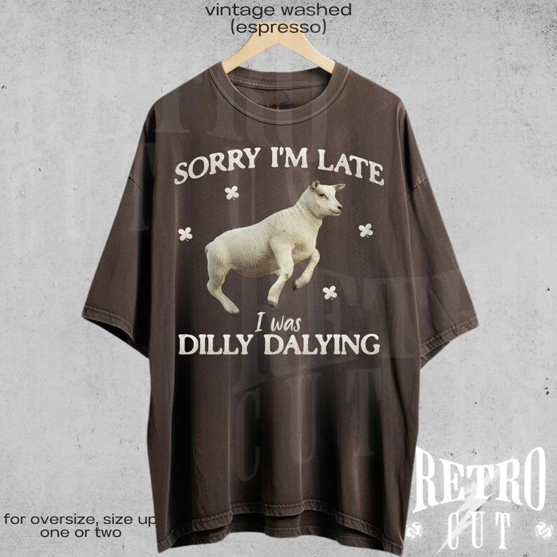 May include: A brown t-shirt with a vintage washed look. The shirt features a white sheep with the text "Sorry I'm Late I was Dilly Dallying" printed on it.