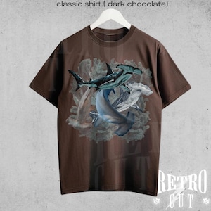 May include: A brown t-shirt with a graphic print of three hammerhead sharks swimming in a coral reef. The text "classic shirt ( dark chocolate )" is printed above the image.