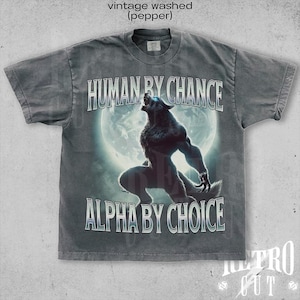 May include: A gray t-shirt with a vintage washed look. The shirt features a graphic of a werewolf howling at the moon with the text "HUMAN BY CHANCE ALPHA BY CHOICE".