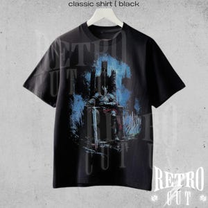May include: Black t-shirt with a graphic print of a figure sitting on a throne in front of a castle. The text "Retro Cut" is printed on the bottom of the shirt.