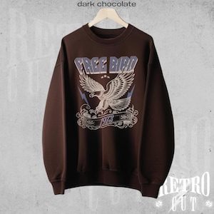 May include: A dark brown sweatshirt with a vintage-style graphic of a flying eagle with the text "FREE BIRD 1973" printed on the front.